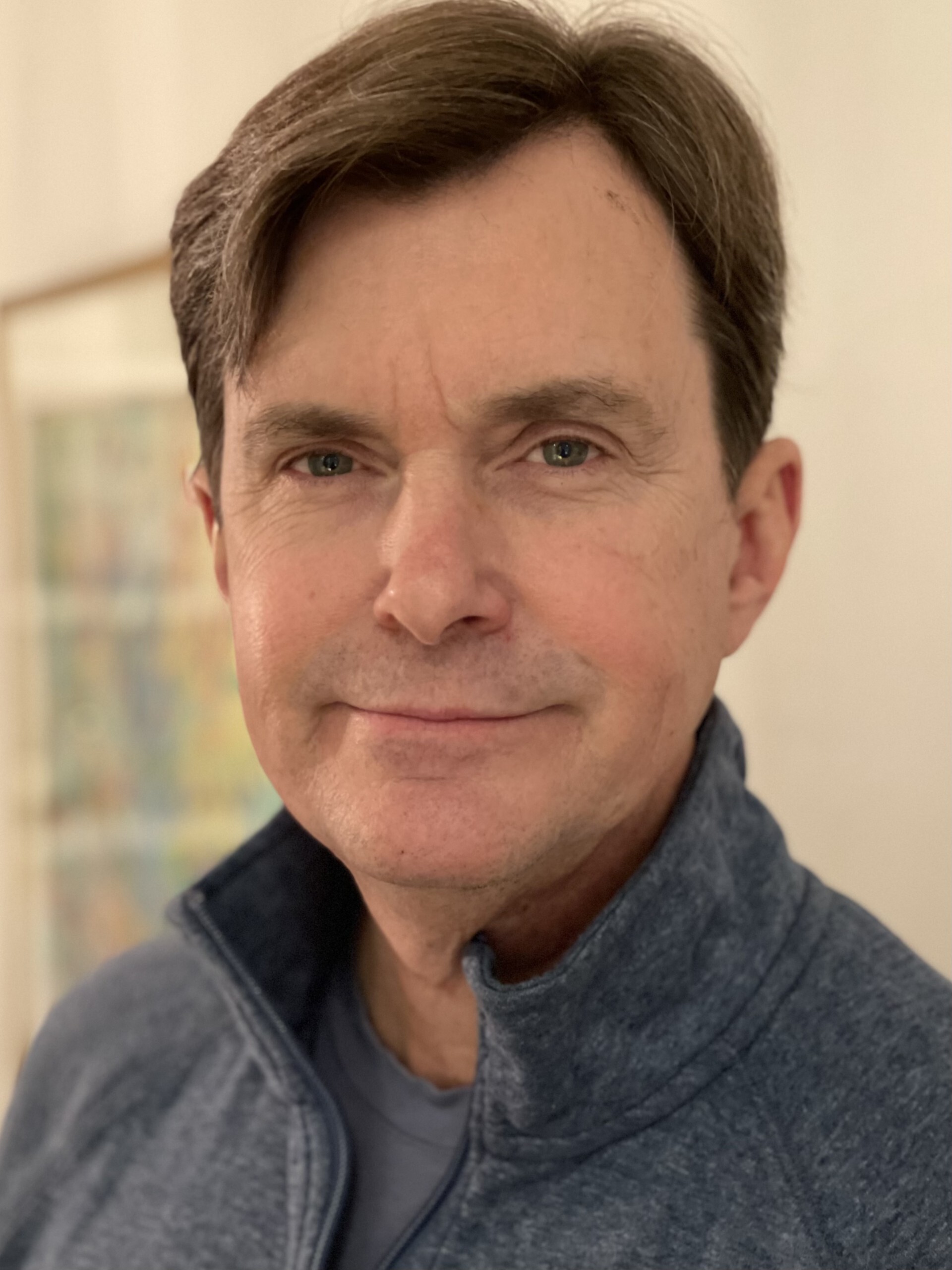 Man with short brown hair and green eyes, wearing a navy zip-up jacket, stands in a well-lit room with a soft background.